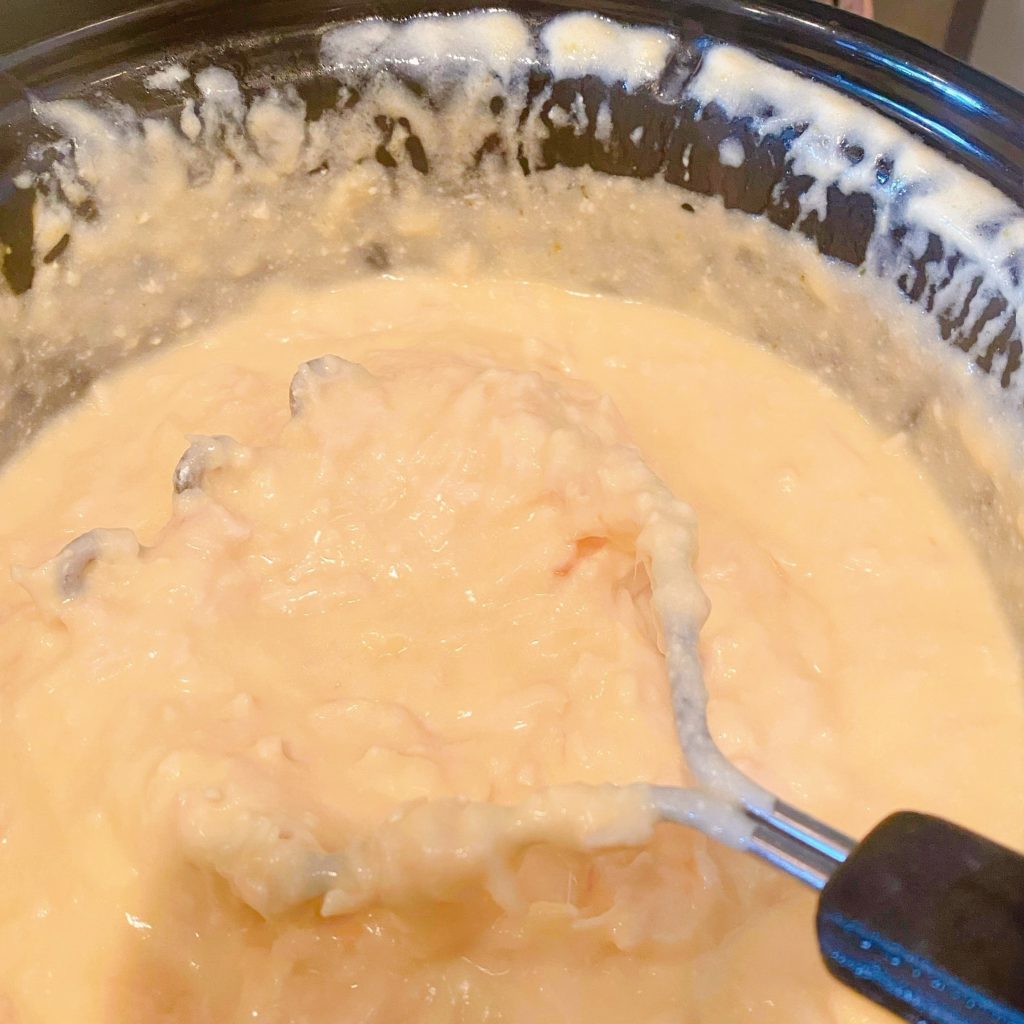 Potato masher shredding chicken in a slow cooker.