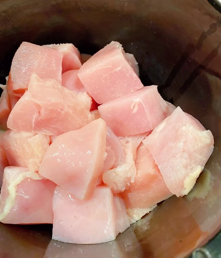 Chicken breast cut into large cubes in a slow cooker.