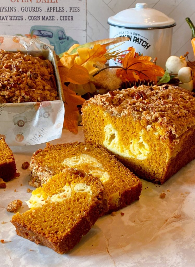 Pumpkin Cream Cheese Bread sliced on a table with a loaf in the background in a loaf pan. 