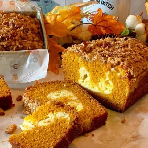 Pumpkin Cream Cheese Bread sliced on a table with a loaf in the background in a loaf pan.