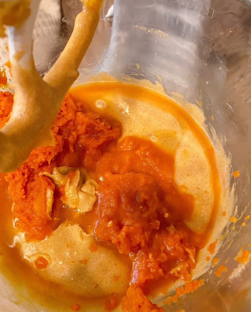 Adding canned pumpkin and water to batter mixture in mixing bowl.