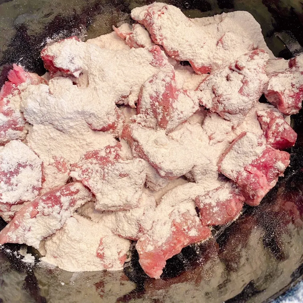 Stew beef covered in flour in slow cooker.