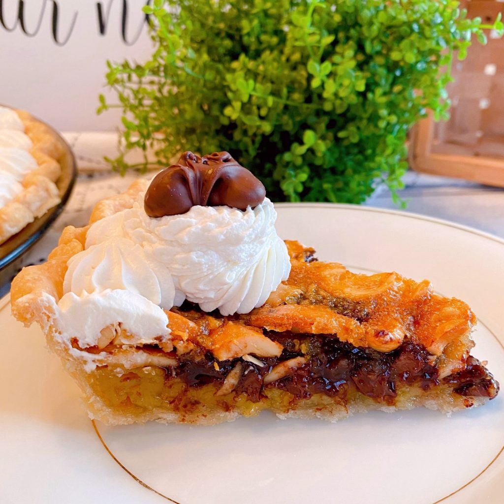 Slice of Chocolate Cashew Pie on a dessert plate with full pie in the background.