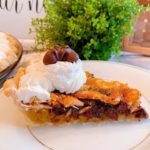 Slice of Chocolate Cashew Pie on a dessert plate with full pie in the background.