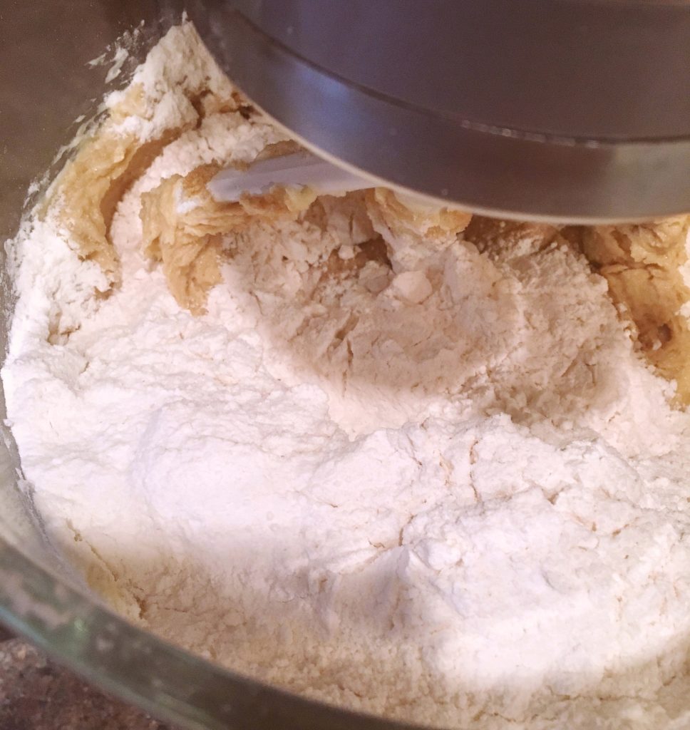 Flour mixture being added to creamed mixture in mixing bowl.