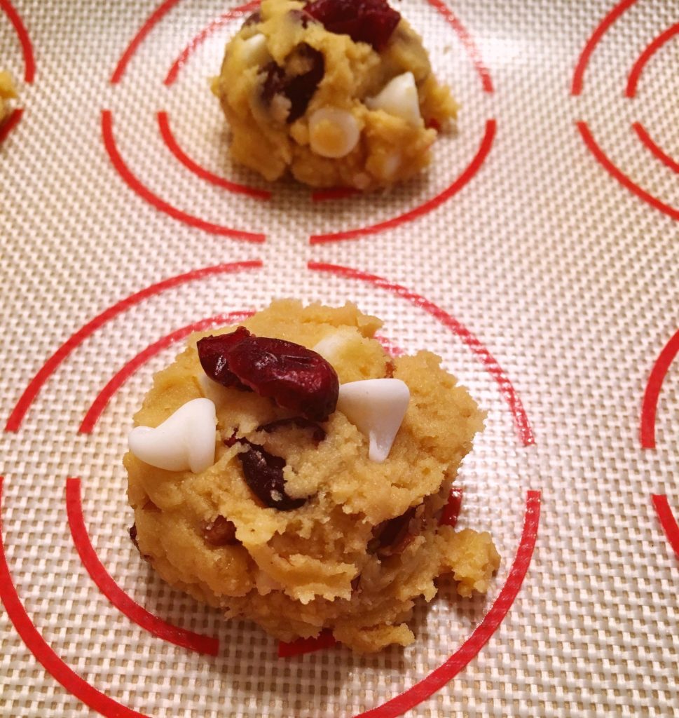 Scoops of cookie dough in baking sheet, lined with silicone baking mat.