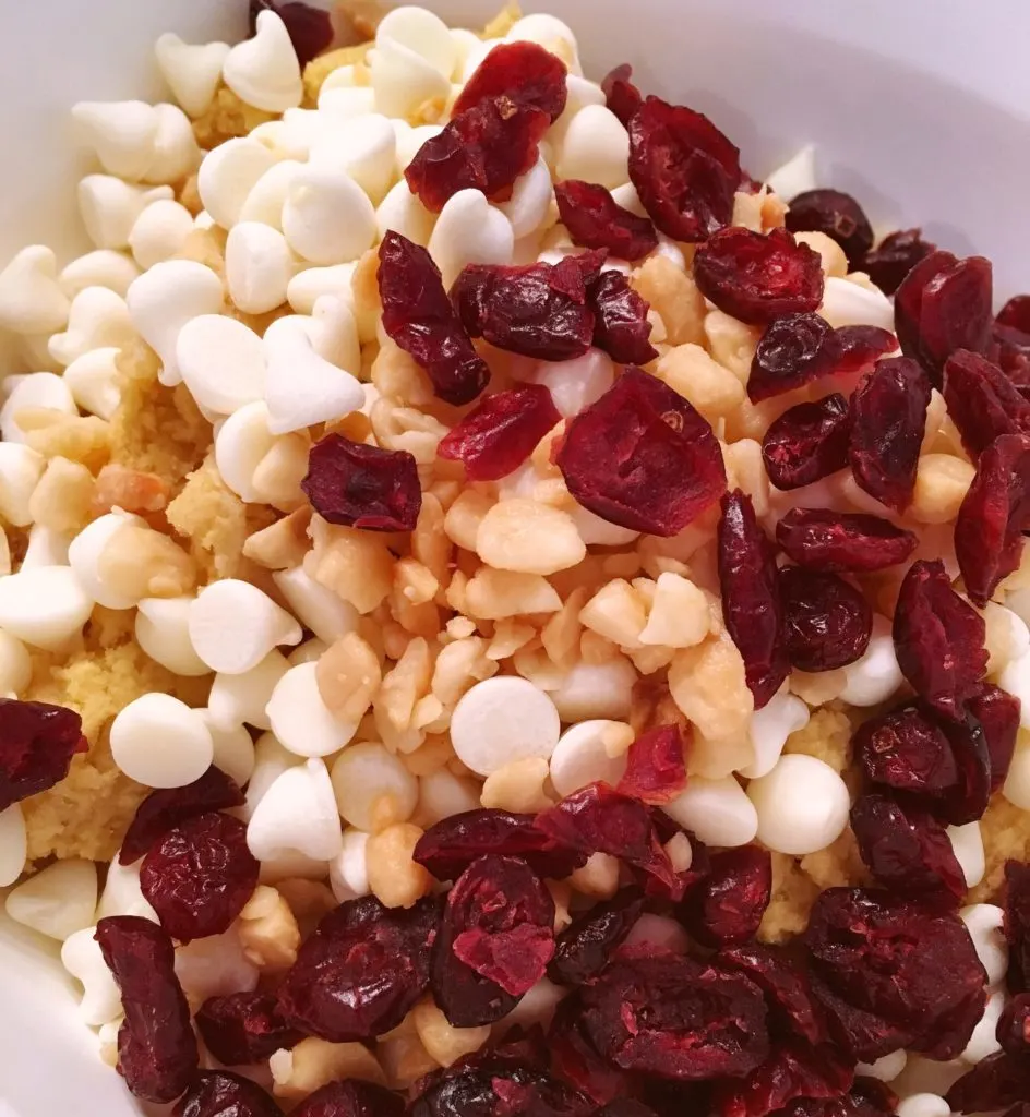 Adding in the white chocolate chips, macadamia nuts, and cranberries to cookie dough in the mixing bowl.