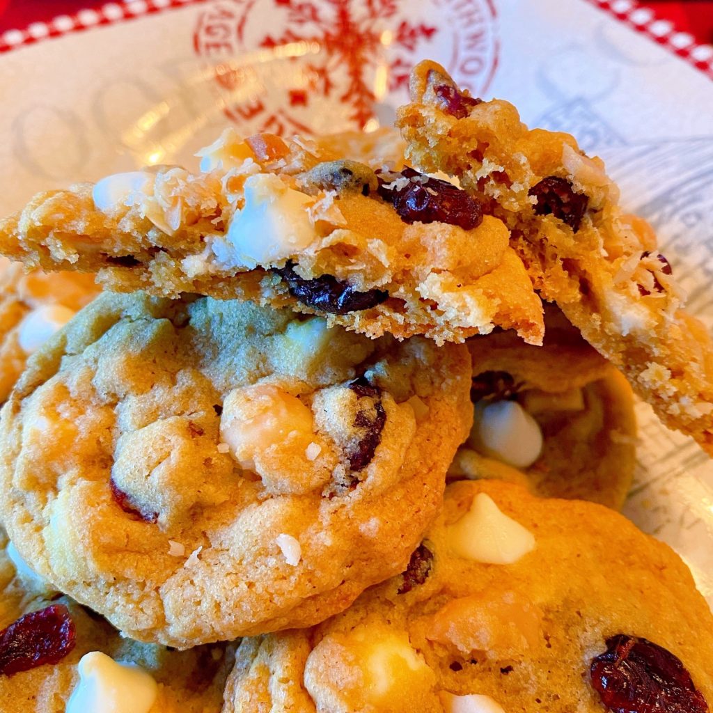 Cranberry White Chocolate Chip Cookies on a plate with one cookie broken in half.