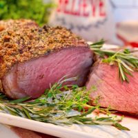 Cross Rib Roast on a white serving latter sliced with fresh herbs surrounding it.