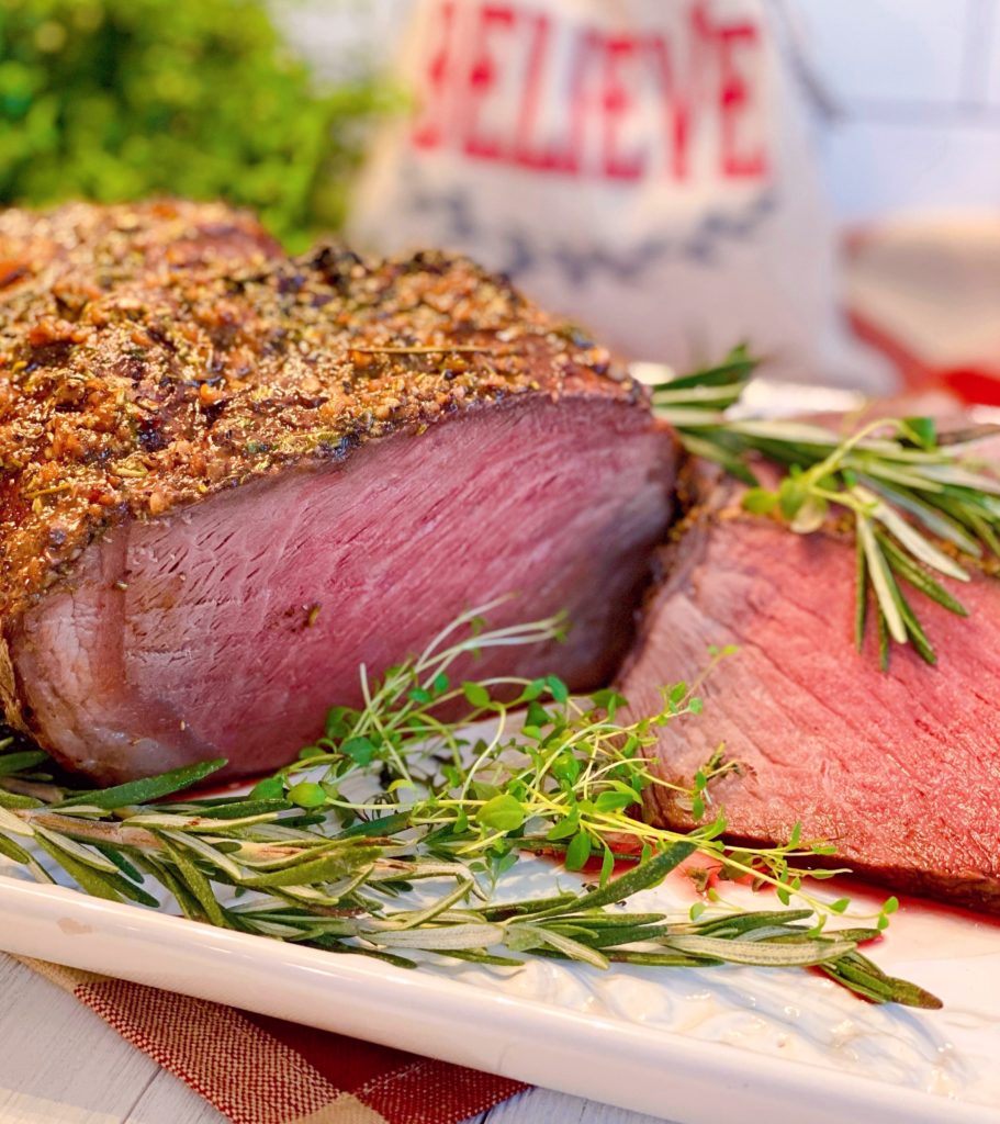 Cross Rib Roast on a white serving latter sliced with fresh herbs surrounding it.