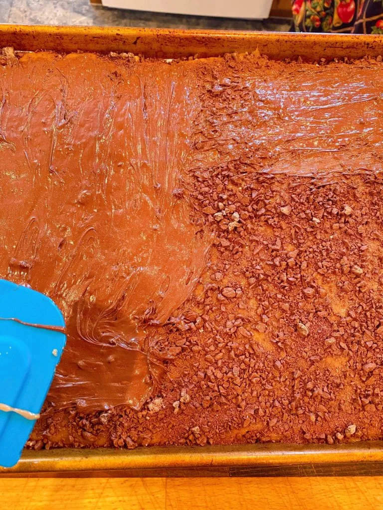 Spreading melted chocolate over toffee in baking sheet.