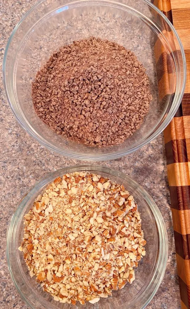 Two bowls on the kitchen counter. One with grated chocolate chips and one with chopped almonds.