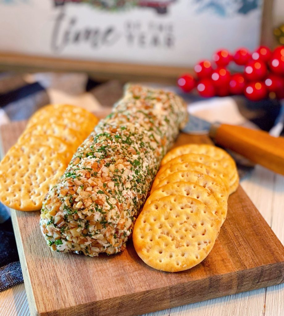 Salmon Party Log on a small cutting board with crackers and holiday decor in the background.