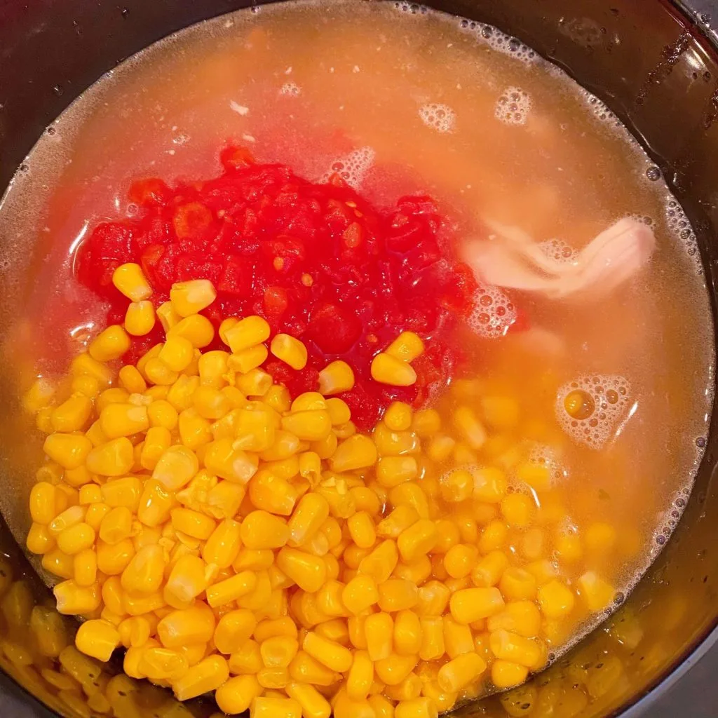 Adding Tomatoes, corn, and garlic to the soup.