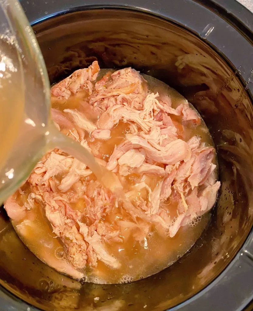 Adding chicken broth and water to slow cooker with chicken.