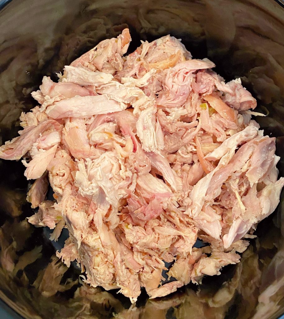 Shredded chicken placed in bottom of slow cooker.