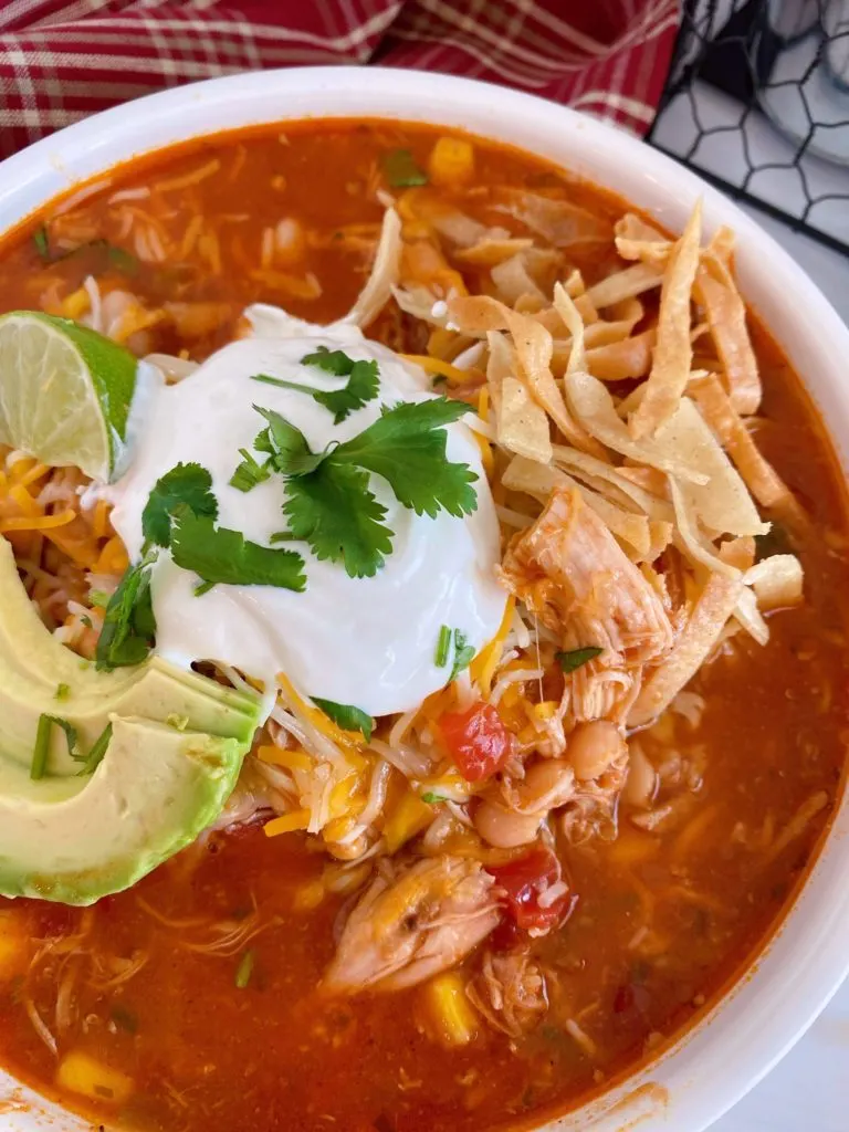 Close up of a bowl full of Chicken Tortilla Soup garnished with fresh avocado sour cream, and tortilla chips.