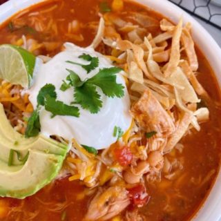 Close up of a bowl full of Chicken Tortilla Soup garnished with fresh avocado sour cream, and tortilla chips.