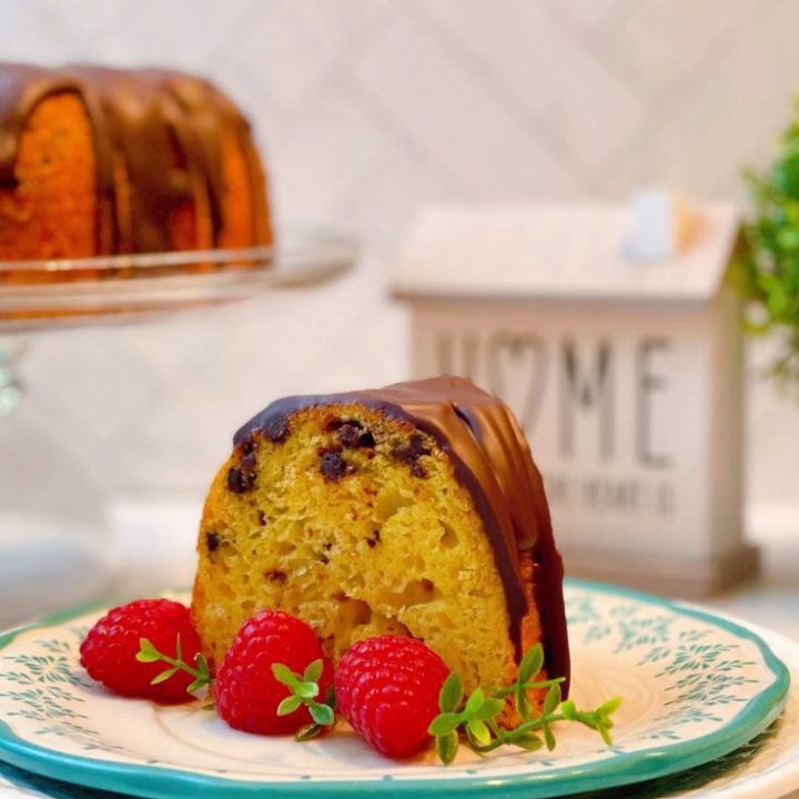 Slice of Vanilla Chocolate Chip Cake with raspberries and whole cake in the background.