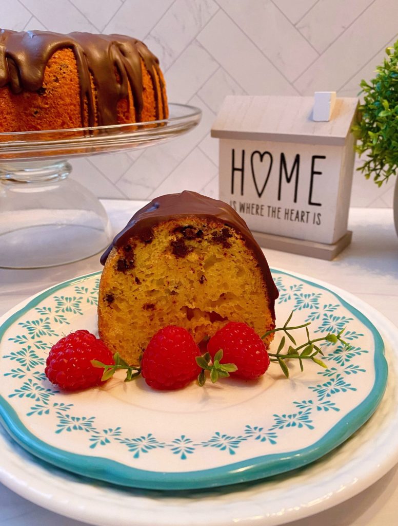 A slice of Vanilla Chocolate Chip Cake with fresh raspberries and the bundt cake in the background.