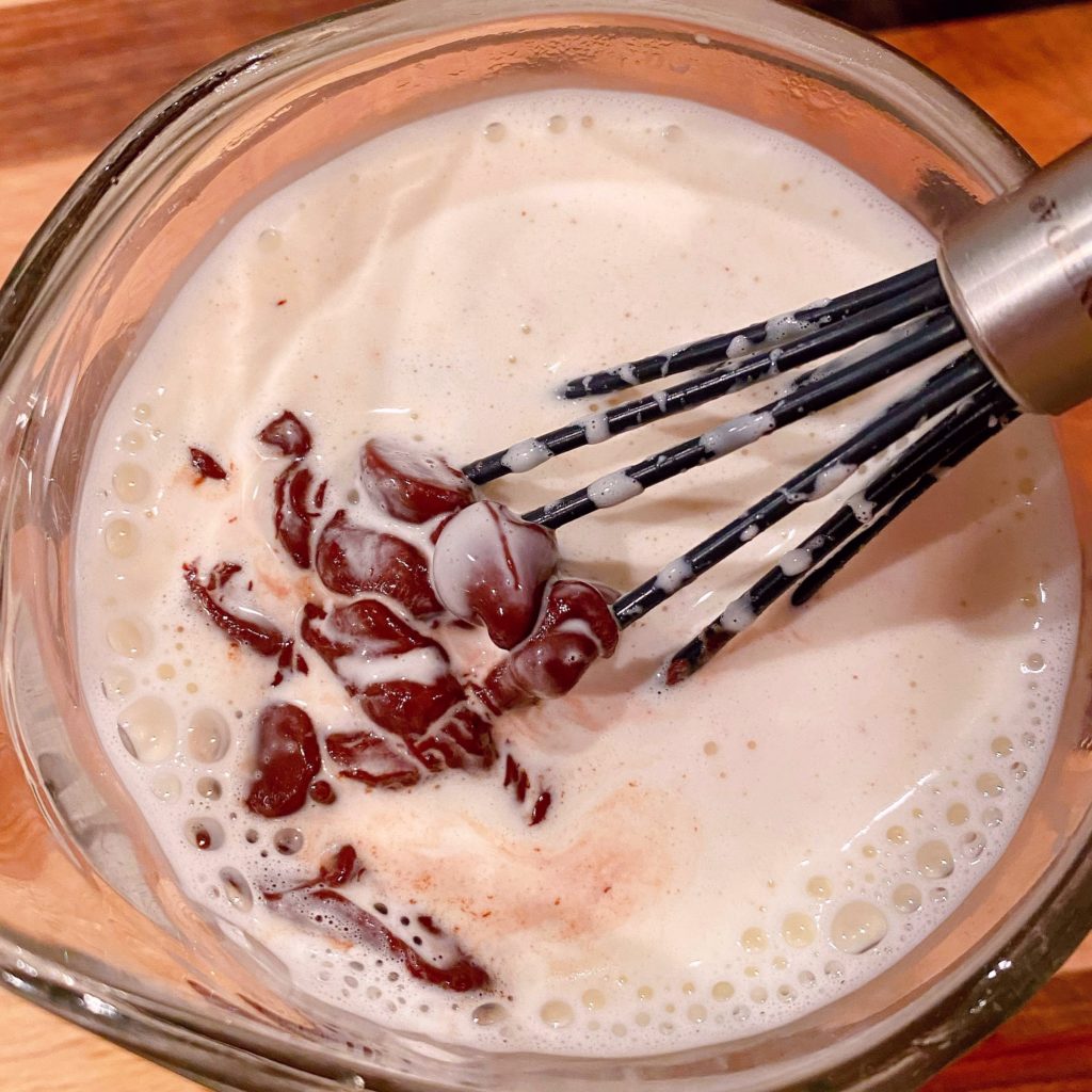 Heavy hot cream and chocolate chips in a microwave safe dish being whisked together to create ganache.