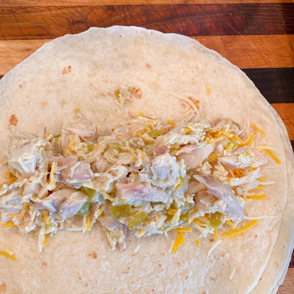 Chicken filling down the center of a flour tortilla for making enchiladas.