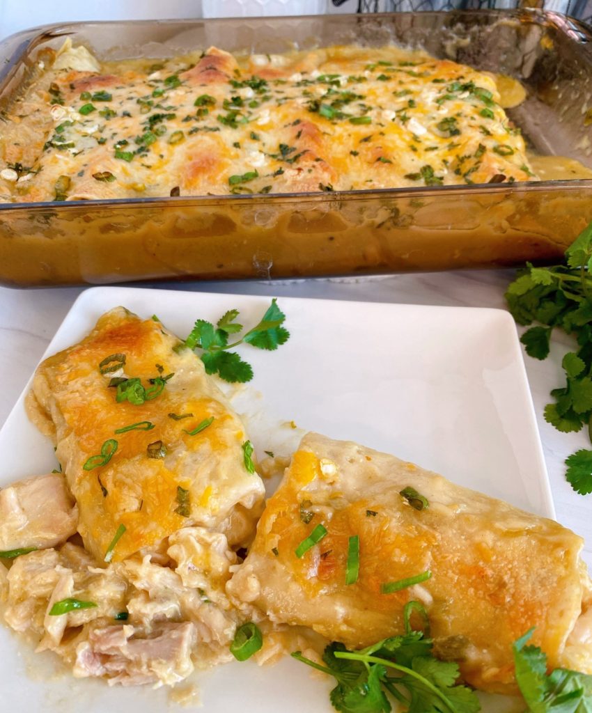 One creamy chicken green chile enchilada on a white palte with enchilada's in a baking pan behind it.