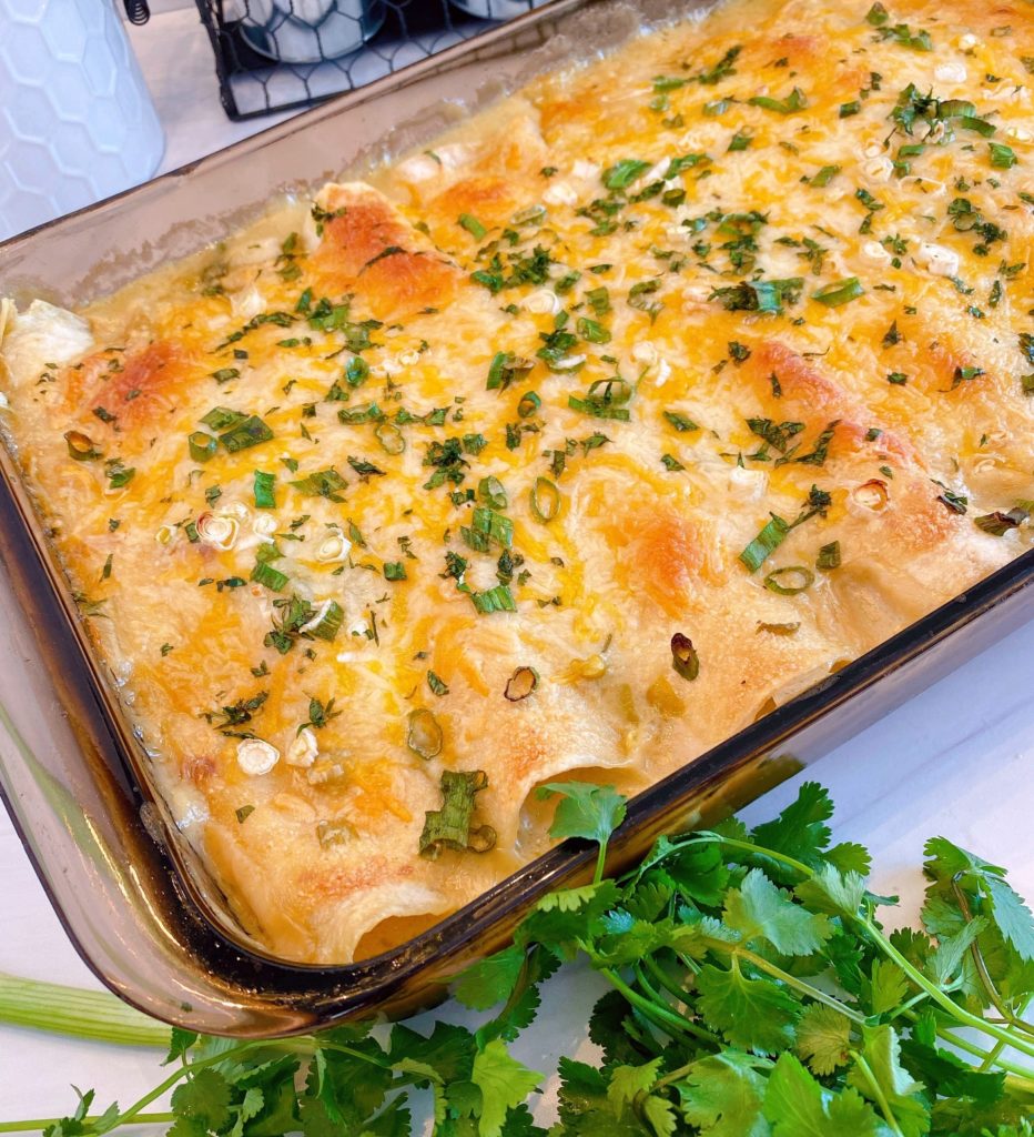 9 x 13 Casserole dish full of Creamy Chicken Flour Enchiladas surrounded by cilantro.