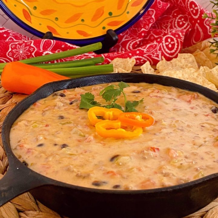 Small Cast Iron Skillet full of Loaded Cowboy Queso with pepper garnish.