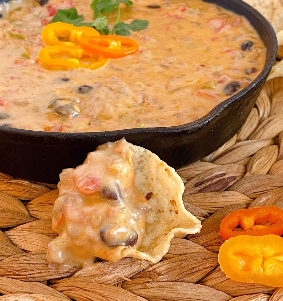 Chip loaded with Cowboy Queso sitting on the table with the pan of queso behind it.