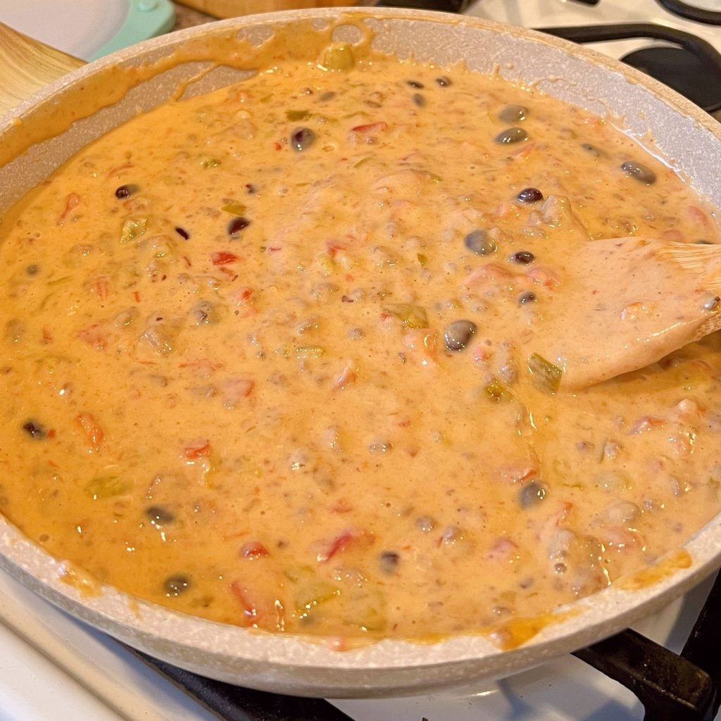 Queso Dip with beans added being stirred on the stove top.