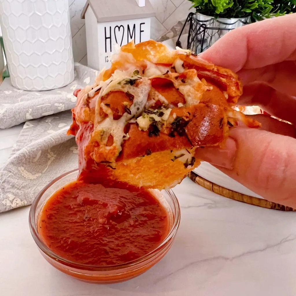 Pizza slider dunked into a dish of marinara sauce.