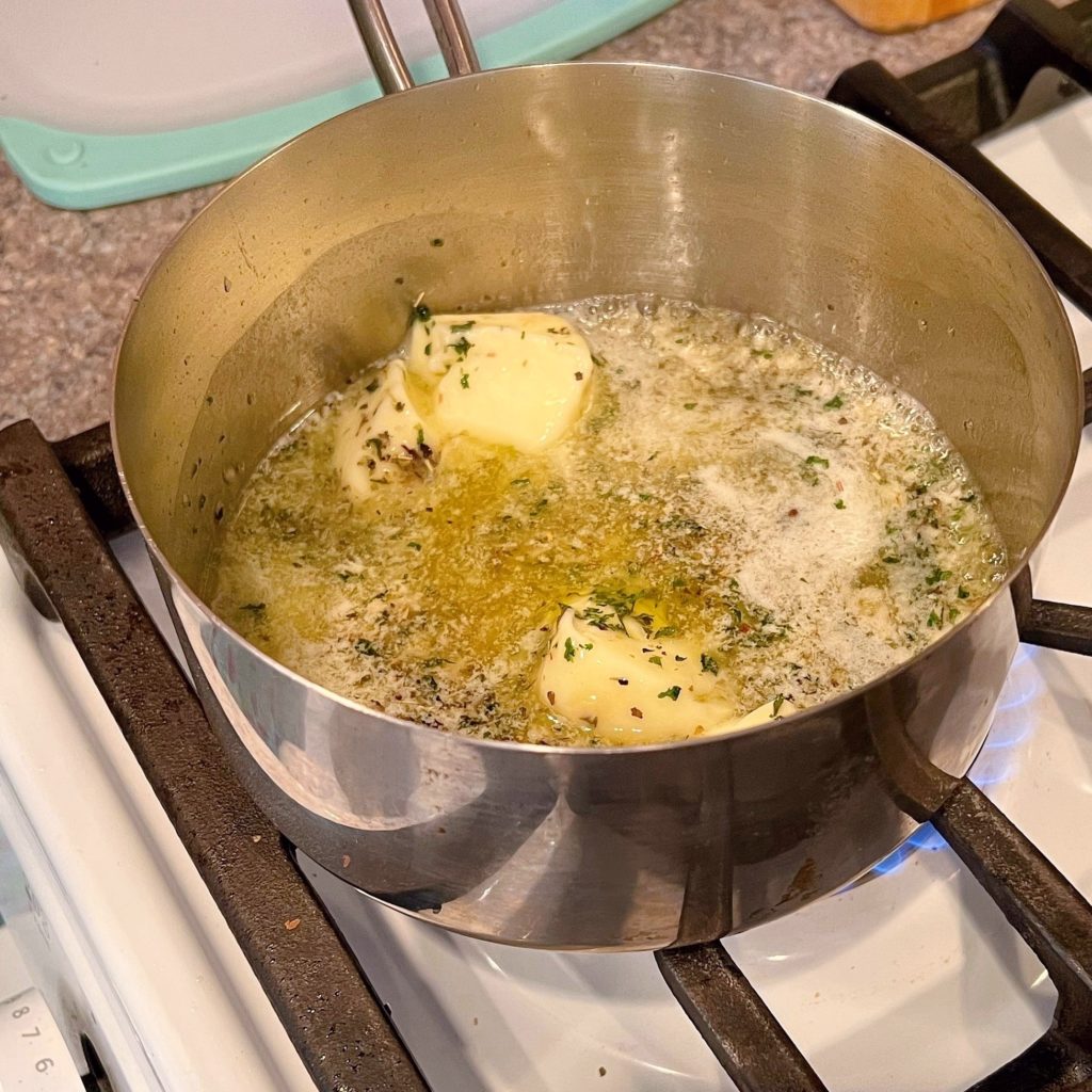 Sauce pan with melted butter, minced garlic and Italian Seasonings on the stove top.