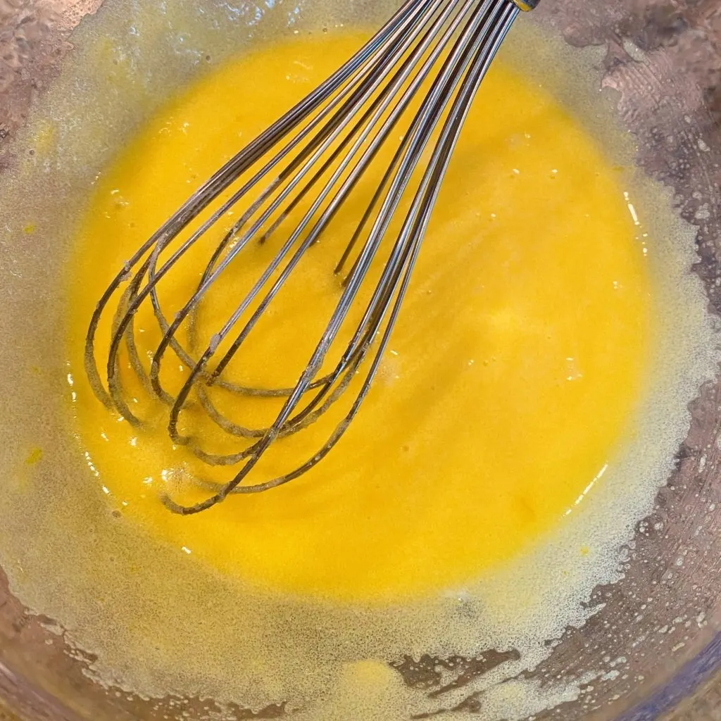 Egg sugar mixture mixed together in a bowl with wire whisk.