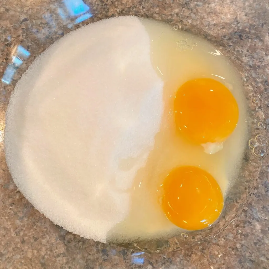 Medium bowl with sugar and two eggs.