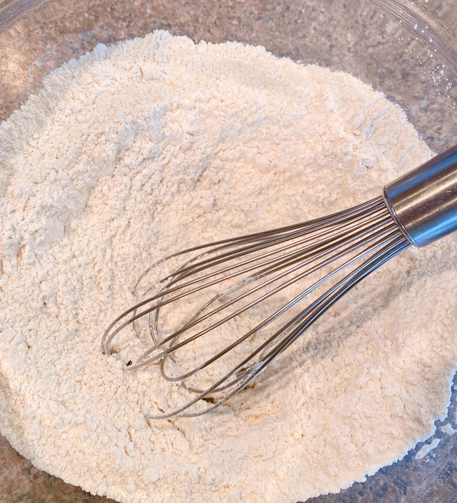 Large glass bowl filled with dry ingredients for muffins and whisk.