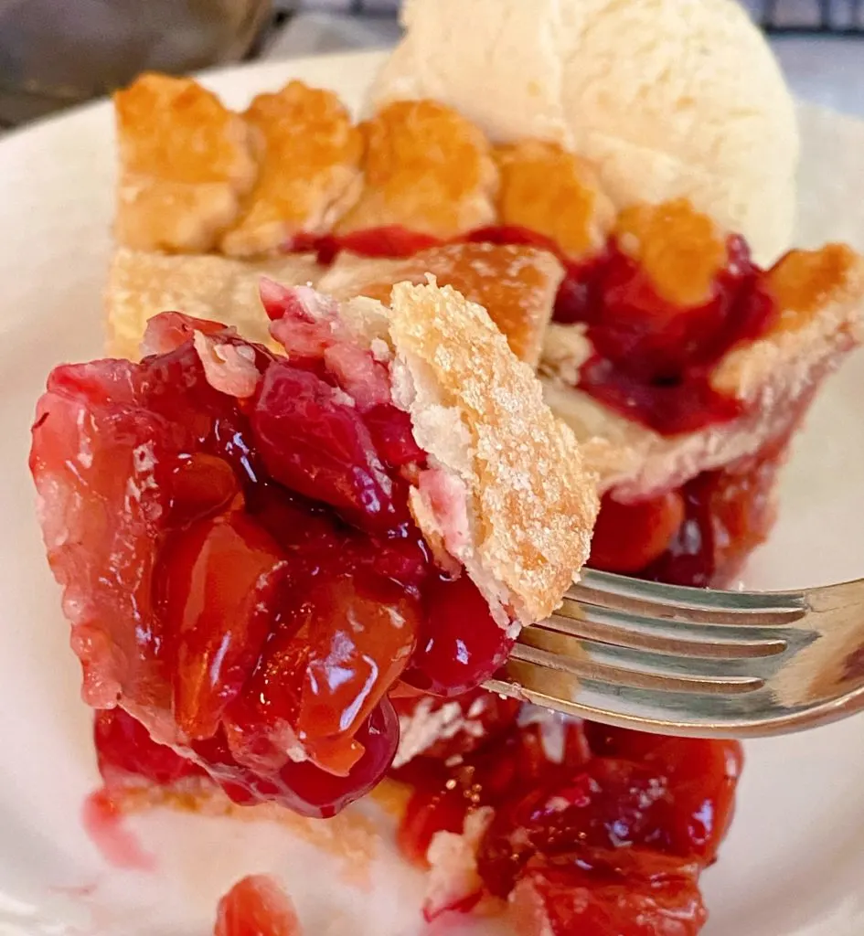 Slice of pie with a bite on a fork with a scoop of vanilla ice cream.