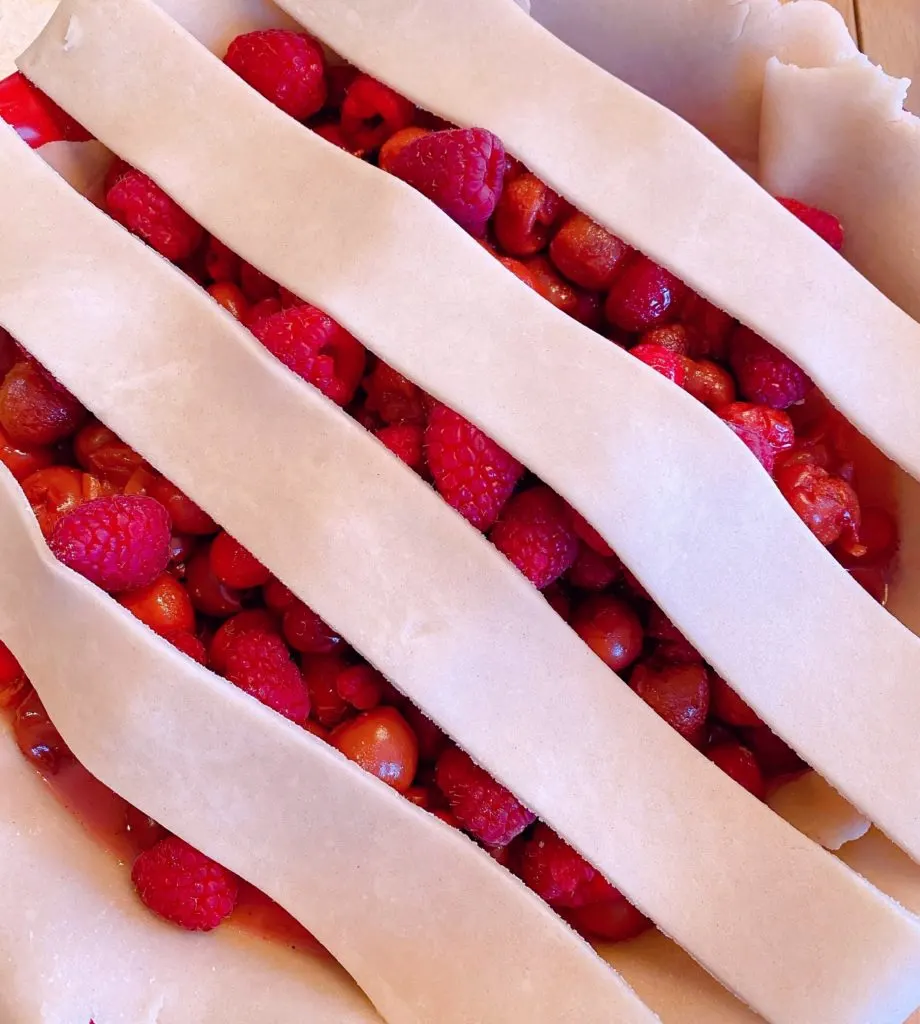 Placing pie crust strips on the top of the pie for a lattice crust.