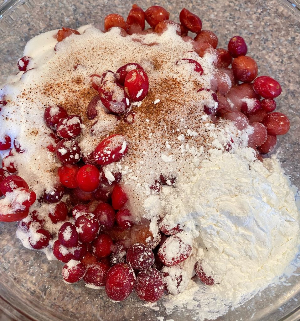 Adding sugar, spices, and corn starch to fruit in large bowl.