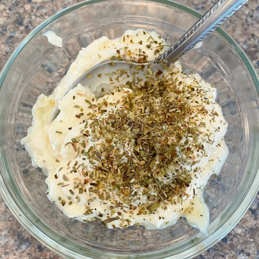 Small bowl with mayonnaise and Italian seasonings with a spoon.