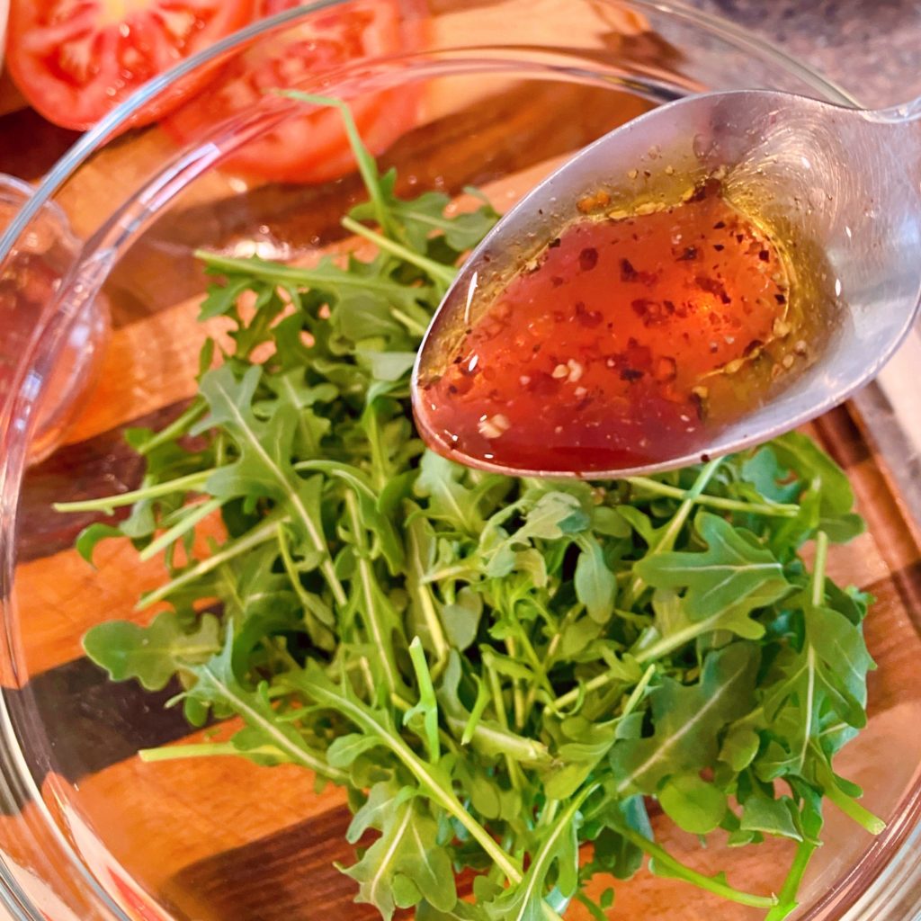 Drizzling arugula with red wine dressing.