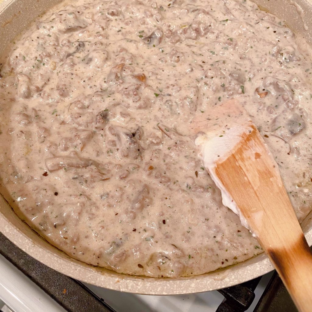 Hamburger gravy for beef stroganoff in skillet simmering on stove top.