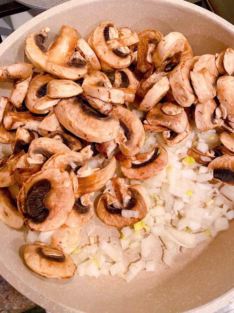 Mushrooms and onions sauting in a large skillet.