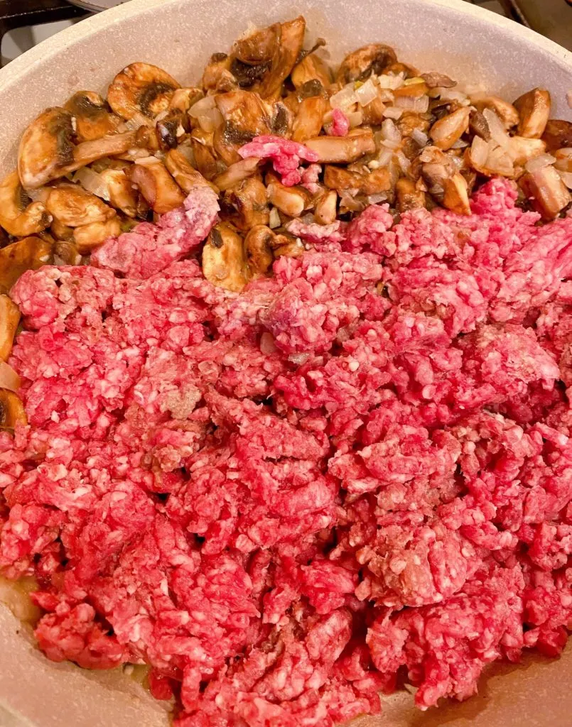 Adding ground beef to mushroom and onions in large skillet on stove top.