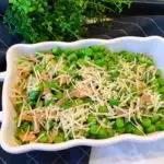 Peas, Prosciutto, and Pine Nuts Side Dish in a white serving dish topped with Parmesan Cheese.