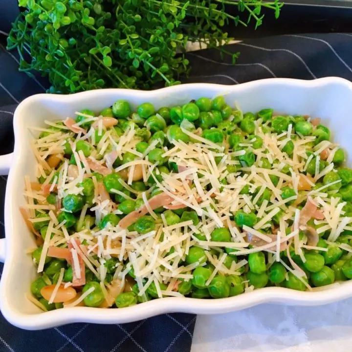 Peas, Prosciutto, and Pine Nuts Side Dish in a white serving dish topped with Parmesan Cheese.