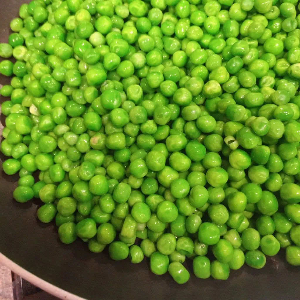 Adding Peas to hot skillet with shallots, garlic, salt, and pepper.
