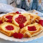 Plate full of Raspberry Cream Danishes with fresh raspberries.