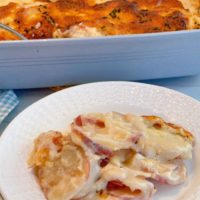 Cheesy Au Gratin Potatoes on a white plate with a casserole dish filled with Creamy Au Gratin potatoes in a casserole.