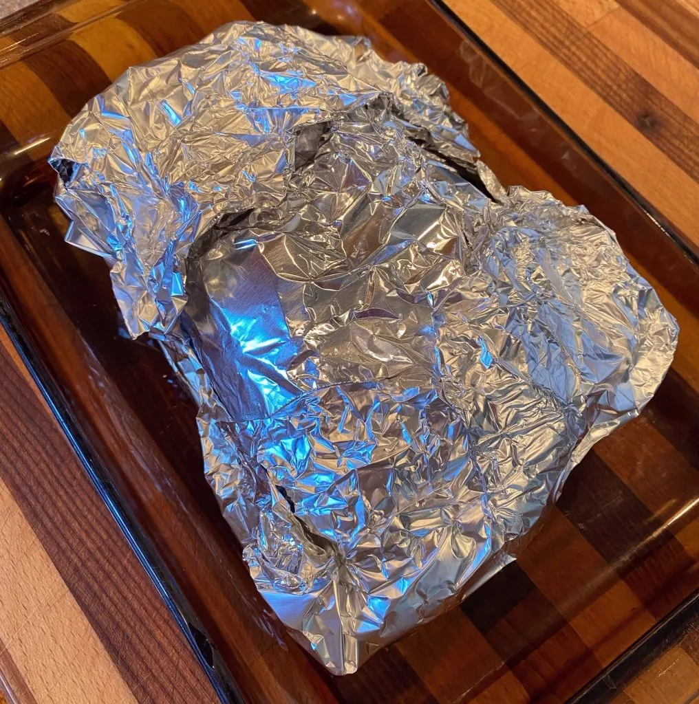 Ham wrapped tightly in foil for baking in a baking dish.